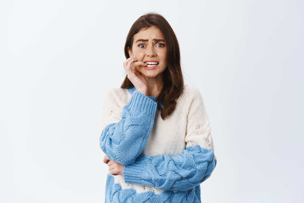 A woman with long brown hair looks worried, biting her nails and clutching her face