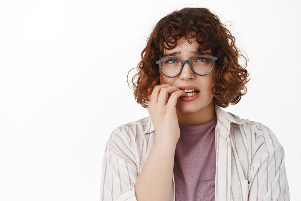 A young girl biting her nails with a worried expression, due to the discomfort of cavities.