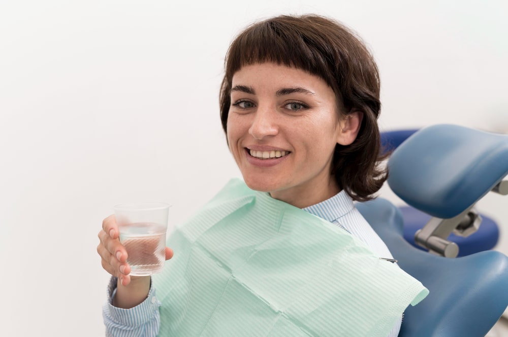 Smiling person in a dental chair holding a cup of water, wearing a dental bib.