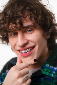 A boy smiling with his hand resting on his neck.