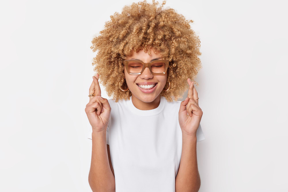 A smiling girl showing her teeth with her fingers crossed in a hopeful gesture.