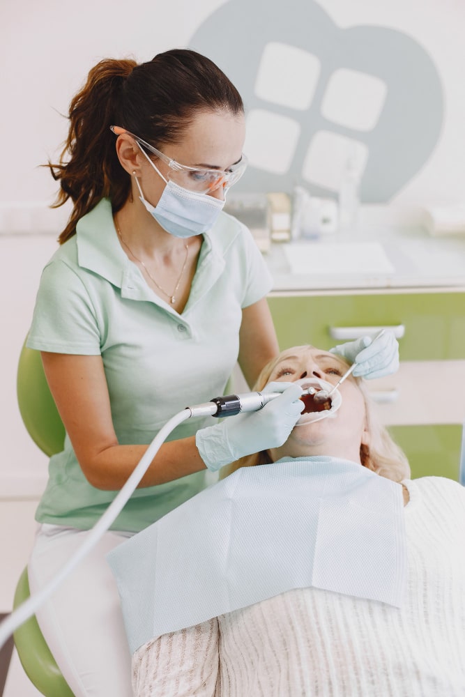 A dentist in protective gear examines a patient in a bright, calm cosmetic dentistry office.