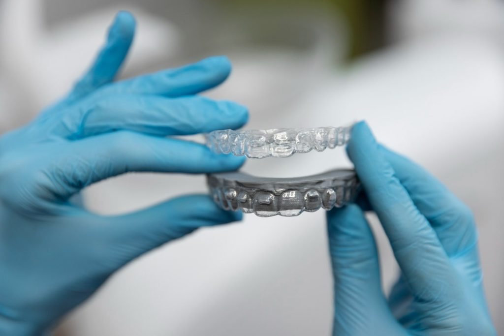 Close-up of gloved hands holding clear aligners used for orthodontic treatment.