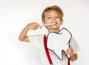 Smiling child holding a large cardboard model of teeth and a toothbrush.