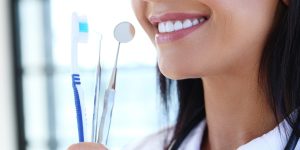 Close-up of a smiling woman holding dental tools and a toothbrush, showcasing clean white teeth and oral hygiene equipment.