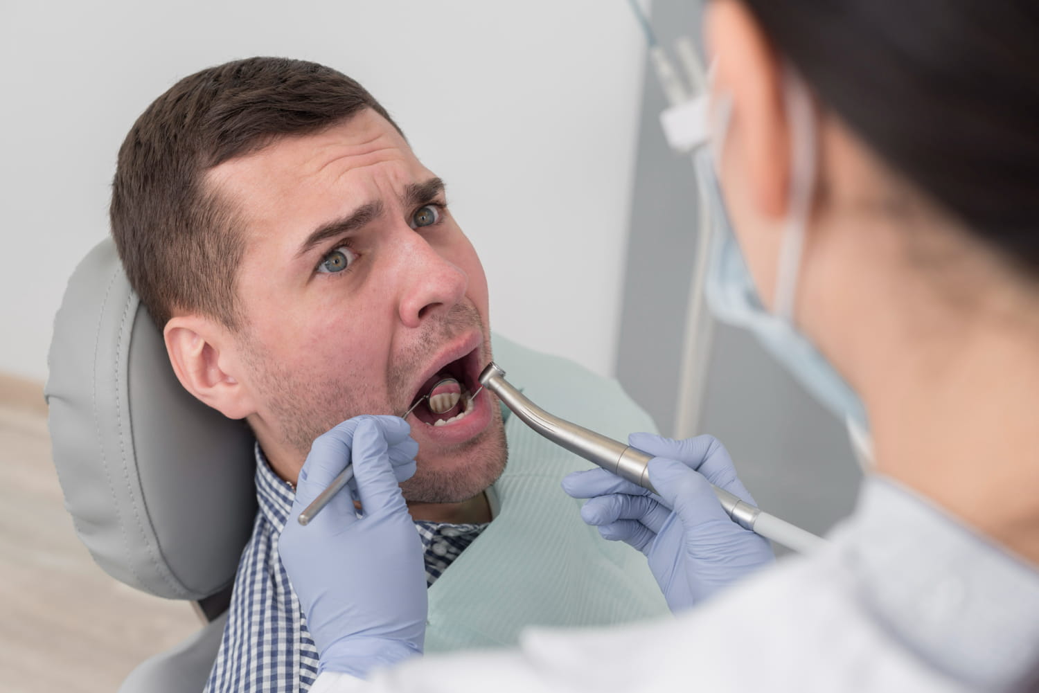 Dentist examining a patient with fractured teeth using dental tools. The patient looks concerned during the check-up.