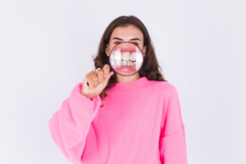 Woman holding a magnifying glass over her teeth, checking for gum recession.