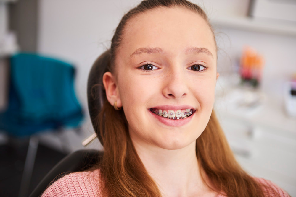 A smiling girl with braces, sitting in a dental chair. She appears cheerful and confident.