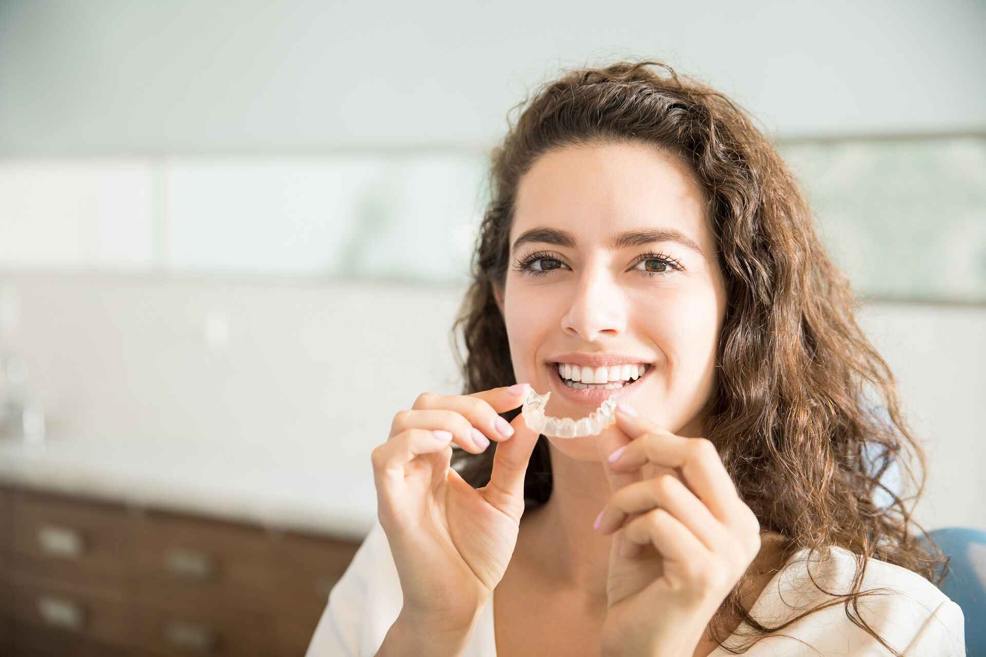 Female patient showing clear aligners at dental clinic for Invisalign comparison